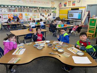four female students stand and smile at the camera. They are holding items they made out of legos. A classroom is in the background.