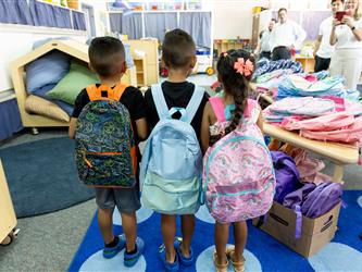 three children showing their backpacks to the camera