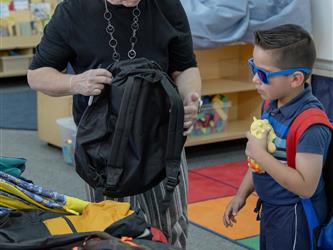 teacher showing a child with sunglasses on a backpack