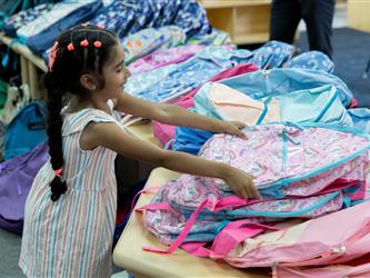 girl holding pink backpack out of a big pile