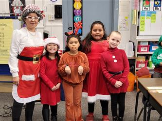 a woman dresses as Mrs.Claus and students dressed as reindeer smiling at the camera