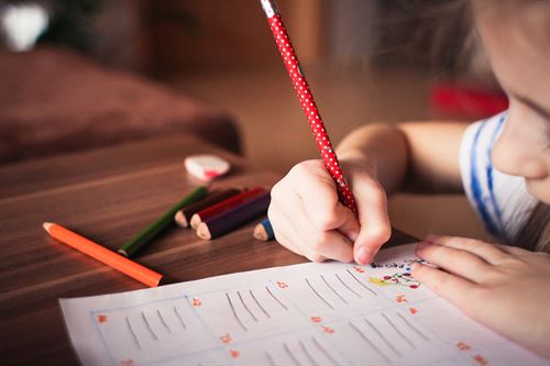 Child sitting at a table with colored pencils writing on a piece of paper